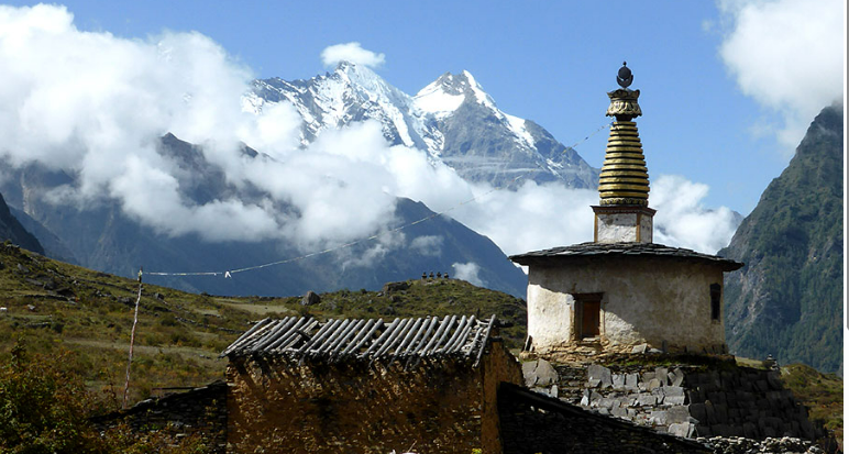 A whitewashed chorten standing beneath snow peaks in the Tsum Valley