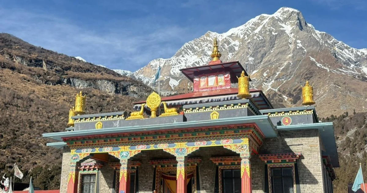 A gompa with gilded roof ornaments and painted pillars, a snow peak rising behind it